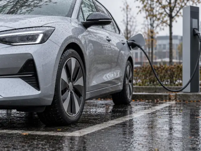 Silbernes Elektroauto an einer Ladesäule auf einem regennassen Parkplatz, im Vordergrund das aerodynamisch geformte Rad